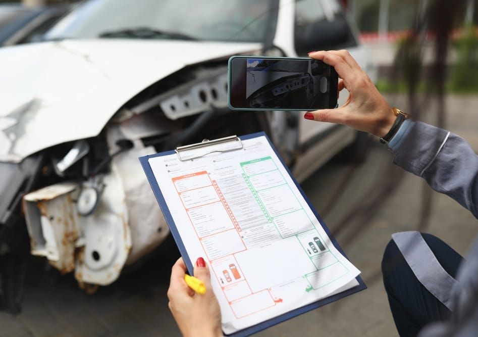 Photo of someone taking a picture of a car accident damage and holding a form on a clipboard
