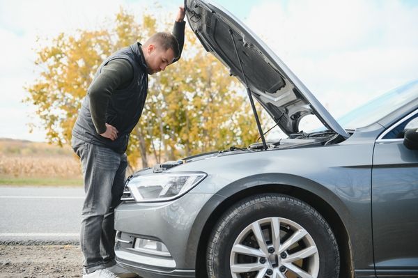 Man repairing a broken car by the road. Man having trouble with his broken car on the highway roadside. Man looking under the car hood. Car breaks down on the autobahn. Roadside assistance concept